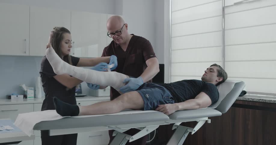 A pair of nurses wrapping bandages around a patients leg in a clinic