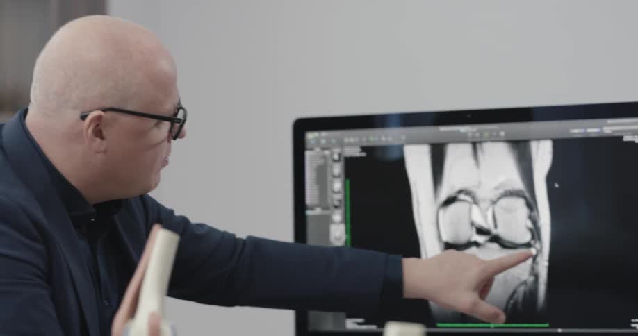 Doctor talks about kneecap and illustrates on mac computer display in the office during daylight