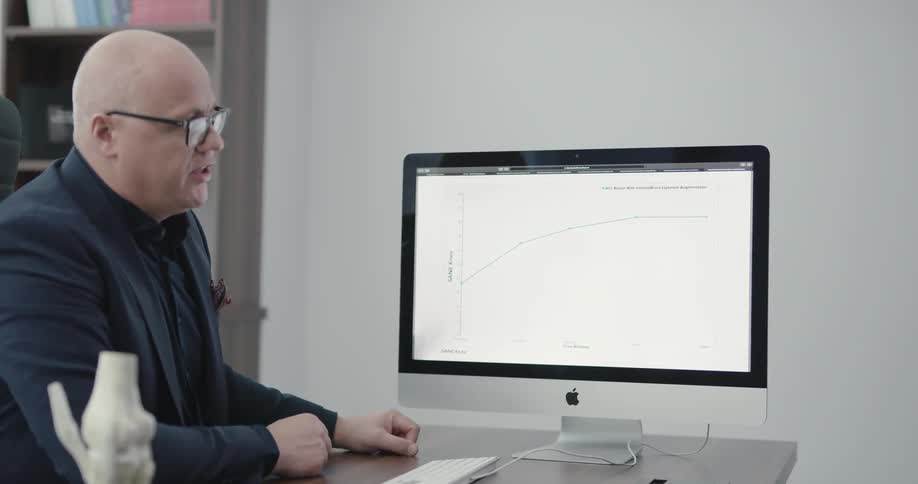 A man sits at his desk talking and turns his computer to show others