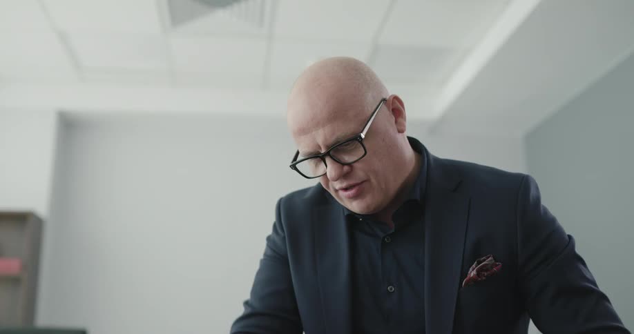 A bald man in a suit coat tests the flexibility of the knee of a man laying on an examination table