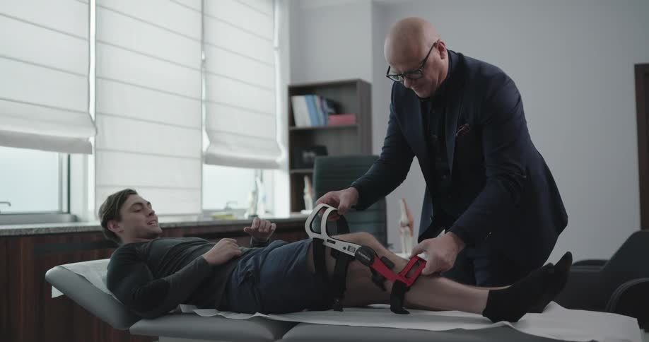 A man lays on a bed while a doctor removes a leg brace