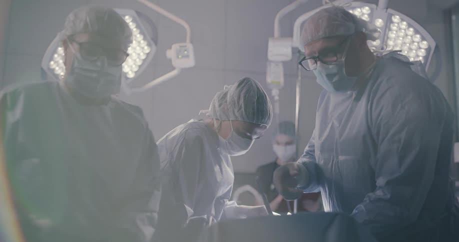 A nurse hands two surgeons medical tools while they are working on a patient