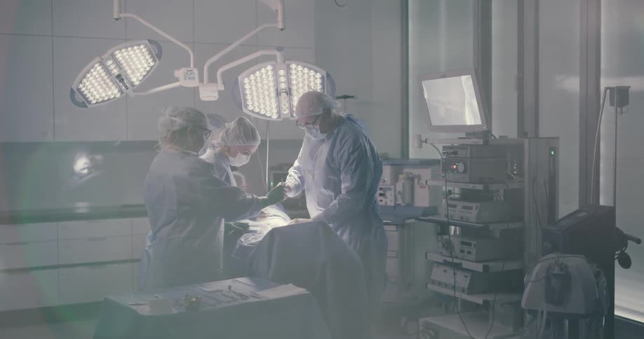 A team of surgeons focus intensely on their patient as the lead surgeon hastily readjusts a surgical light while making an incision