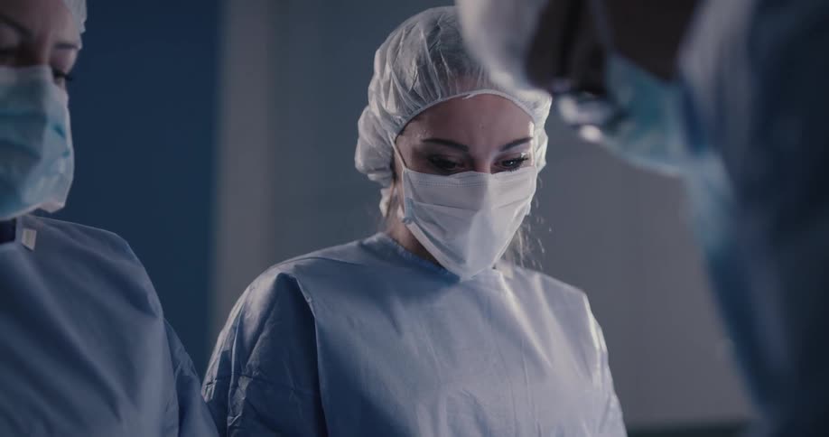 A nurse in an operating room looks up when the surgeon stands up straight