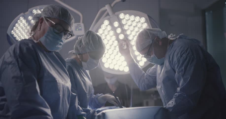 A doctor and nurses stand over an operating table and work on a patient