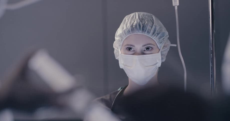 A female medical professional wears a surgical mask while holding a mask over the mouth and nose of a patient in order to deliver anesthesia to them