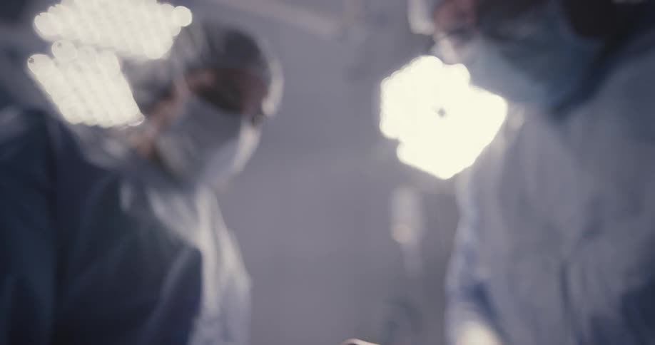 Two medical professionals pass instruments back and forth during a surgery