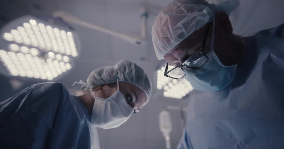 A surgeon uses medical instruments in the operating room with nurses helping him
