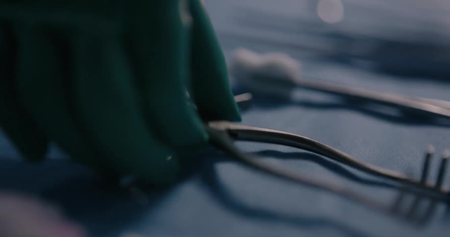A surgeon picks up a tool with a gloved hand in an operating room