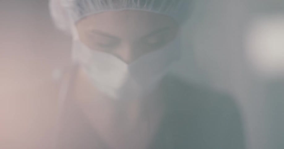 A woman in scrubs and a mask looks up and then down