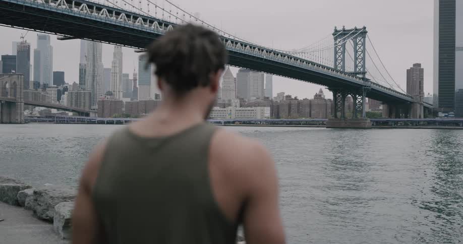 Black man stands on the promenade and looks at the manhattan bridge and new york city during daylight