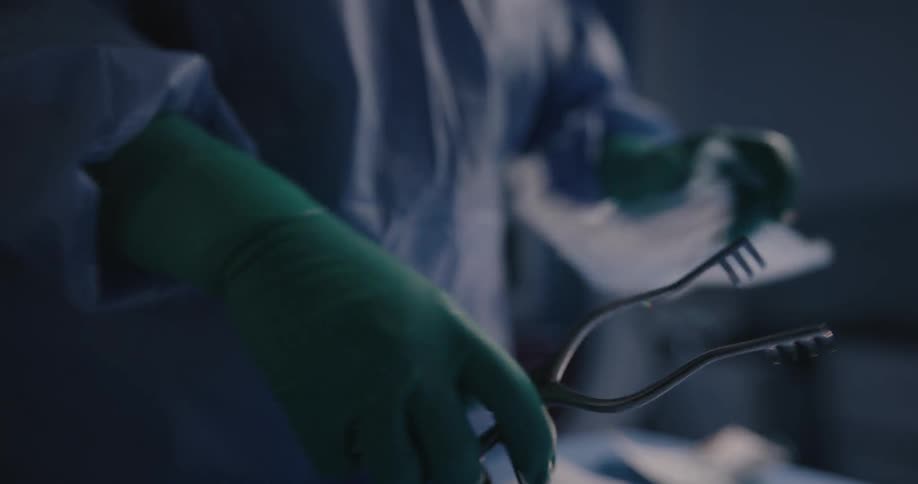 A surgeon removes operating tools from a package while wearing gloves and scrubs in an operating room