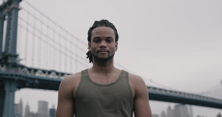 Man stands outdoors with suspension bridge and downtown in the background