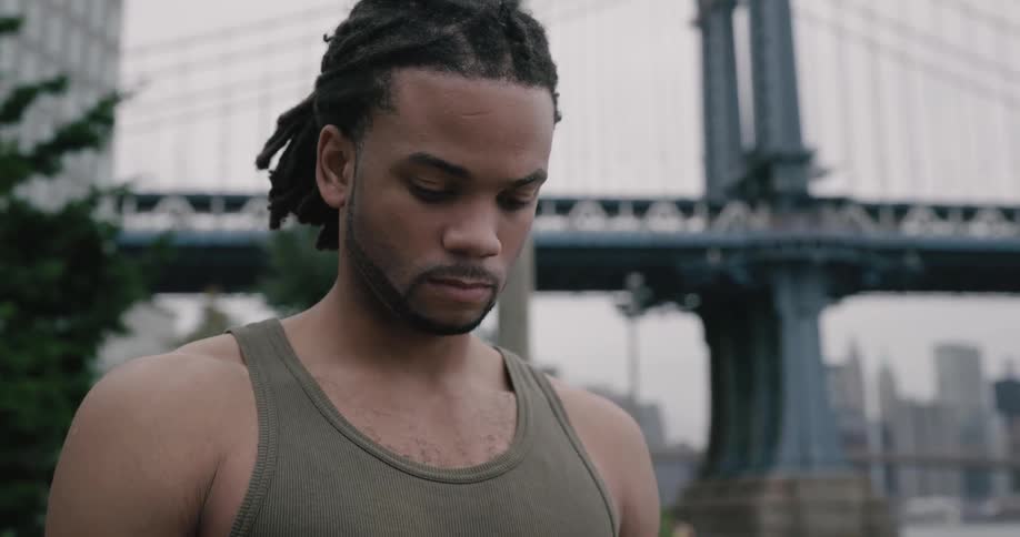 A black man with tank top stand under the brooklyn bridge