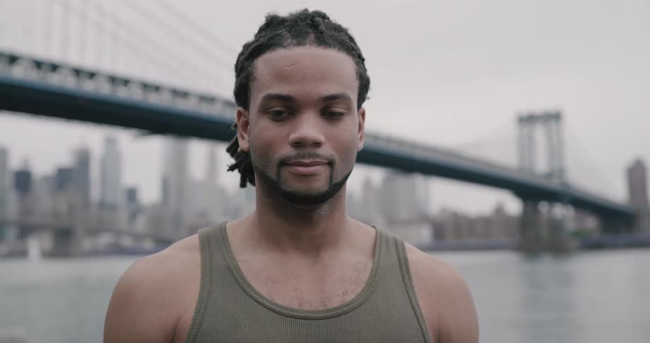 Blackman looks at the camera with the view of manhattan bridge and new york city on a cloudy day