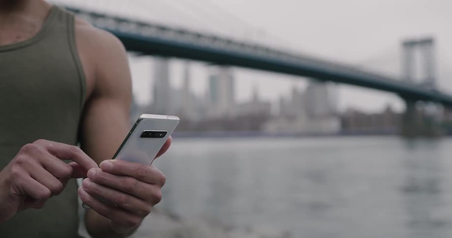 Buffed man texting on phone near brooklyn bridge