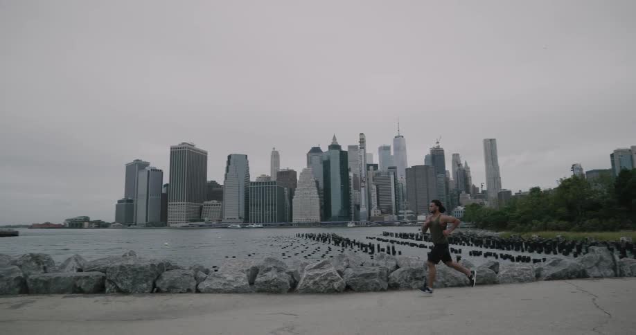 A black man runs in a park by the ocean with a city in the background