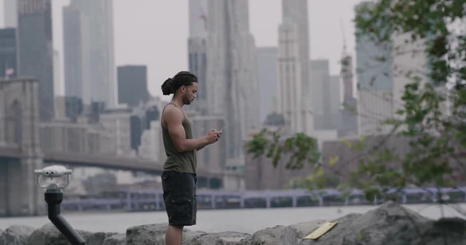 Man uses smartphone on the promenade and looks at new york city during daylight