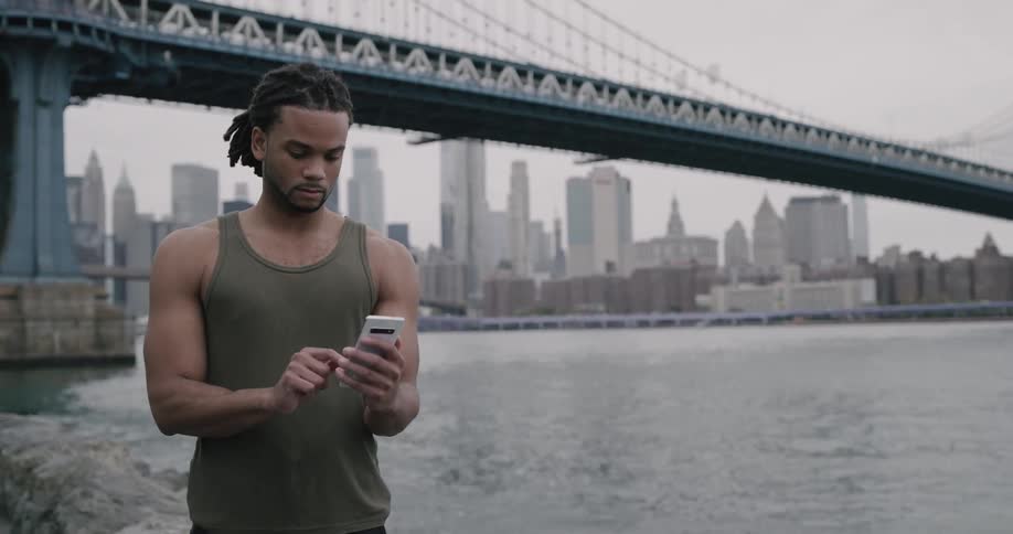Black man texting on the phone under brooklyn bridge