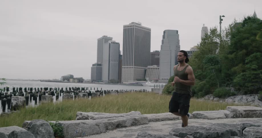A black man with dreads runs in a park overlooking a skyline