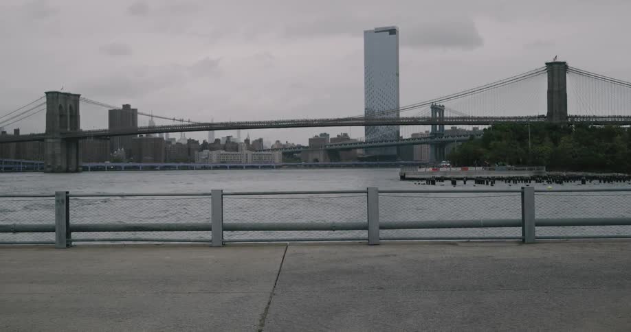 Black man runs along on the promenade next to the river across manhattan bridge and brooklyn bridge on a cloudy day