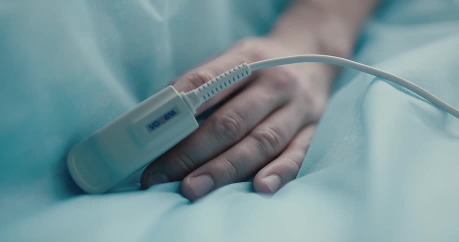 A patient lies in bed with an oxygen saturation monitor on their hand