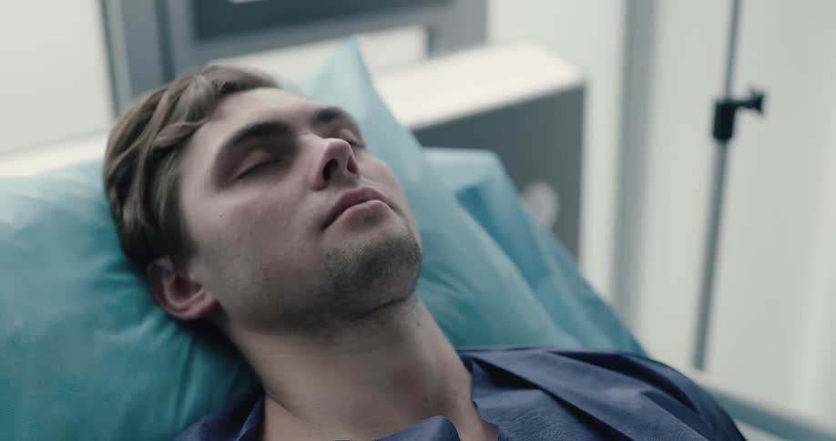A white male is lying on a hospital bed with his eyes closed