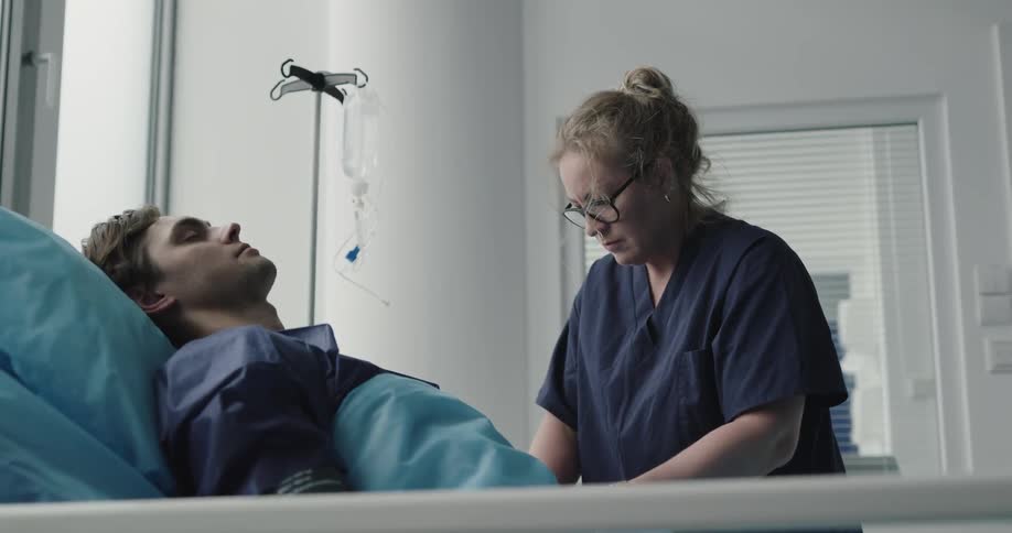 A female nurse cares for a male patient who is laying on a hospital bed