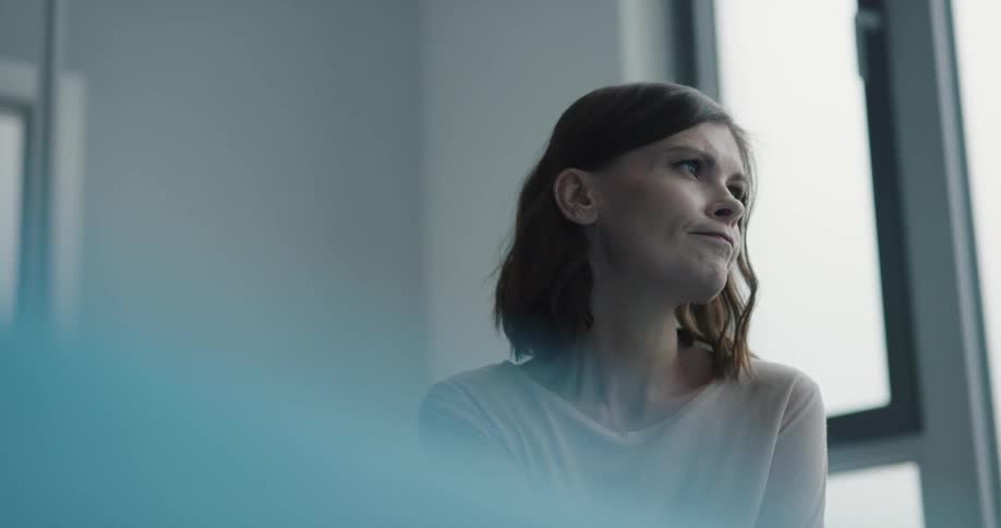 Woman looks out window then stands and walks away
