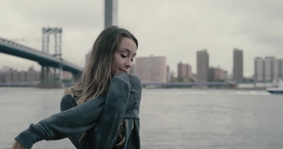 A woman stretches by the water near a bridge