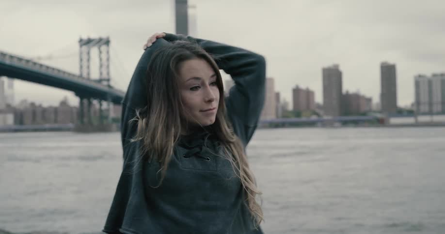 A young woman doing stretches next to a bay in a large city