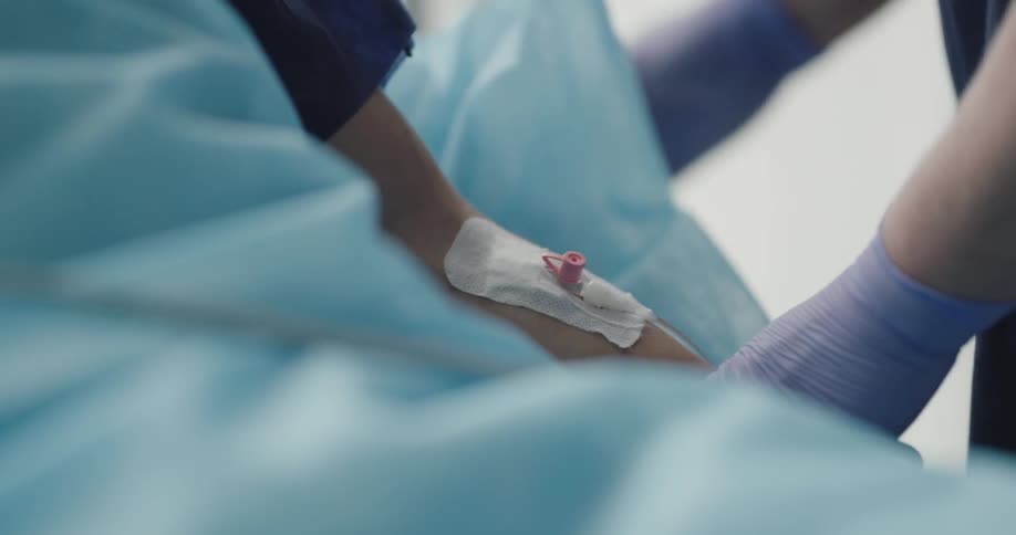 A medical professional wearing gloves prepares a fixed intravenous injection port in the arm of a patient