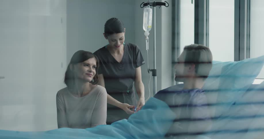 A nurse checks a patients iv bag as he chats with a visitor