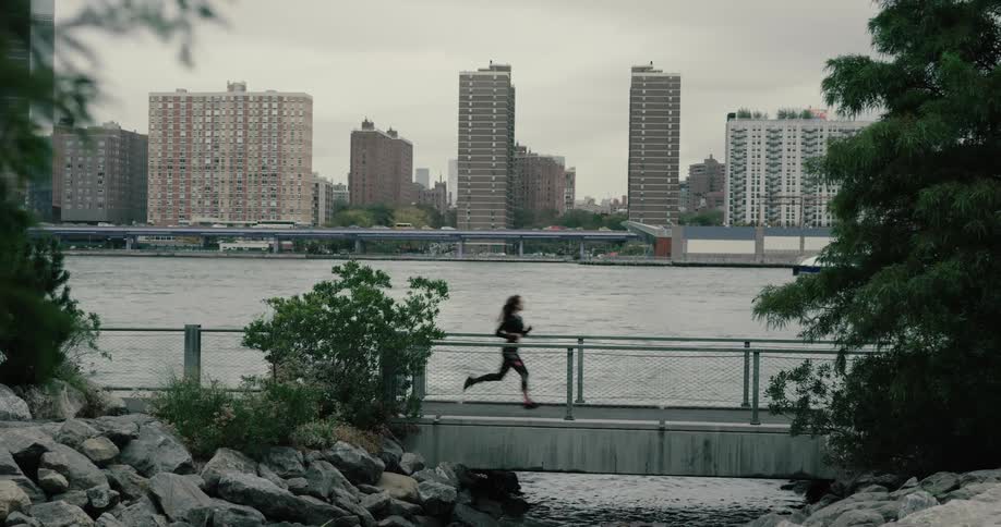 Woman runs along on the promenade next to the river across new york city on a cloudy day