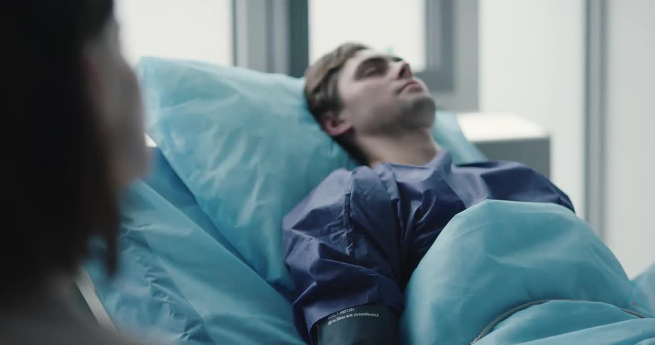 Woman sits by bed of unconscious patient with pressure cuff on his arm