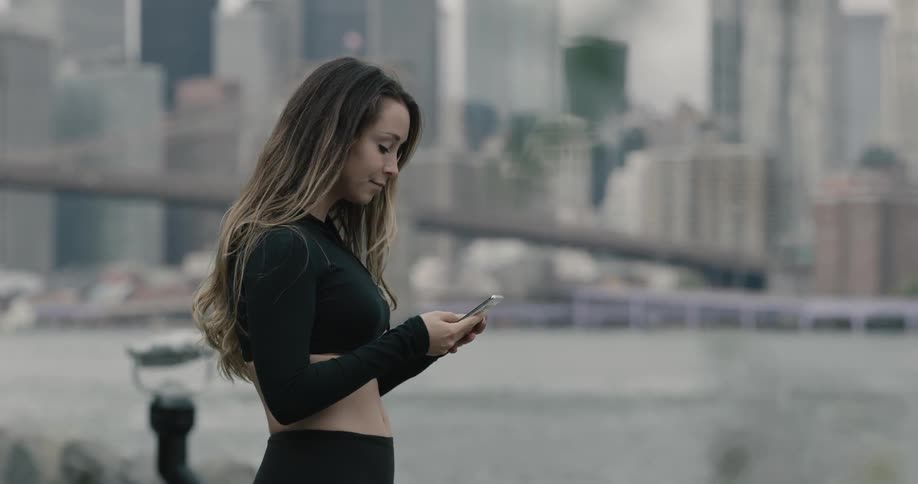 Woman runs along on the promenade and takes a break to wear bluetooth earphones next to the sea across the city on a cloudy day