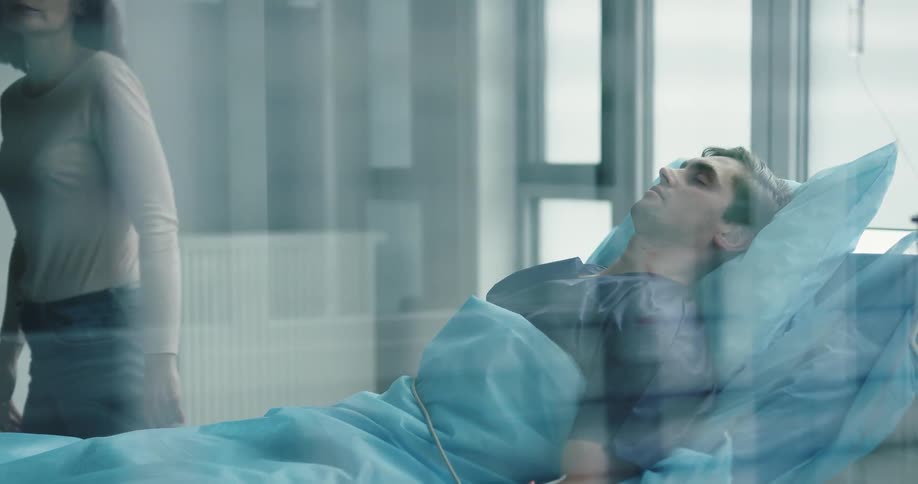 A woman leaving her seat next to a man sleeping in a hospital bed