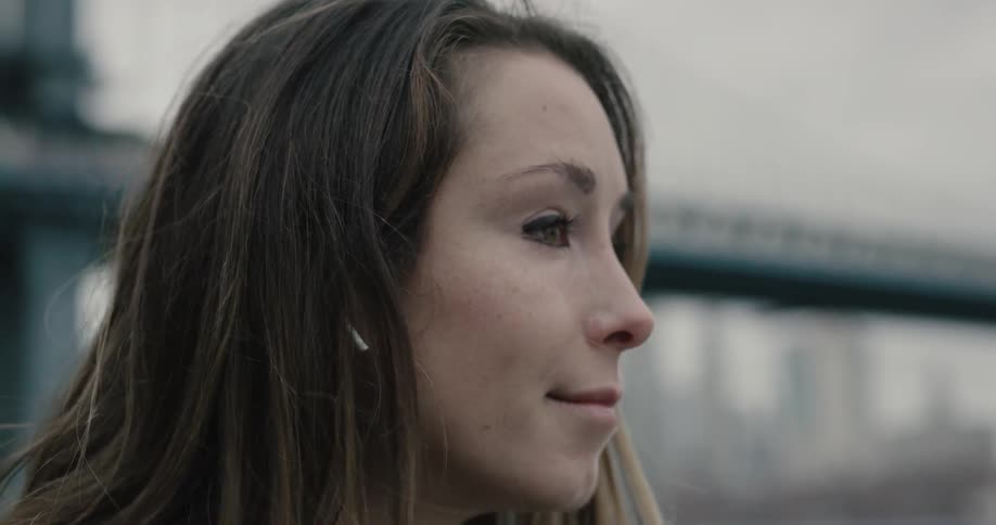 Woman stands outdoors near bridge scrolling through mobile phone