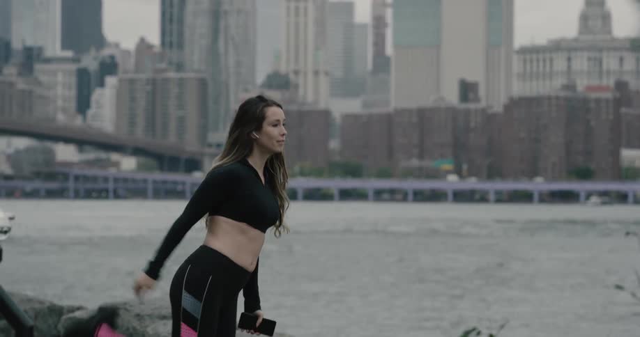 A woman is stretching with her phone by the water