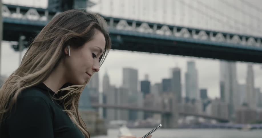 Woman looks at her cellphone as she stands near a bridge