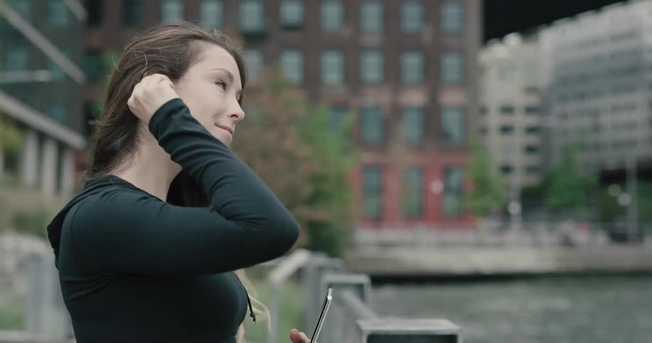Woman takes a break to look around and listen to music then starts running along on the promenade next to the river