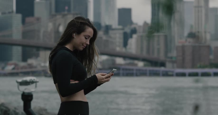 A female jogger stopping to adjust her earbuds and check her phone