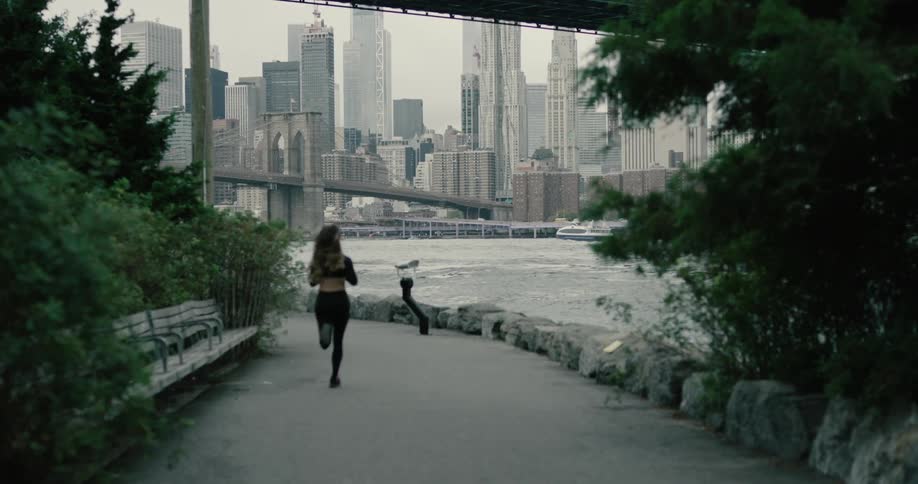 A woman is jogging past the water near the city