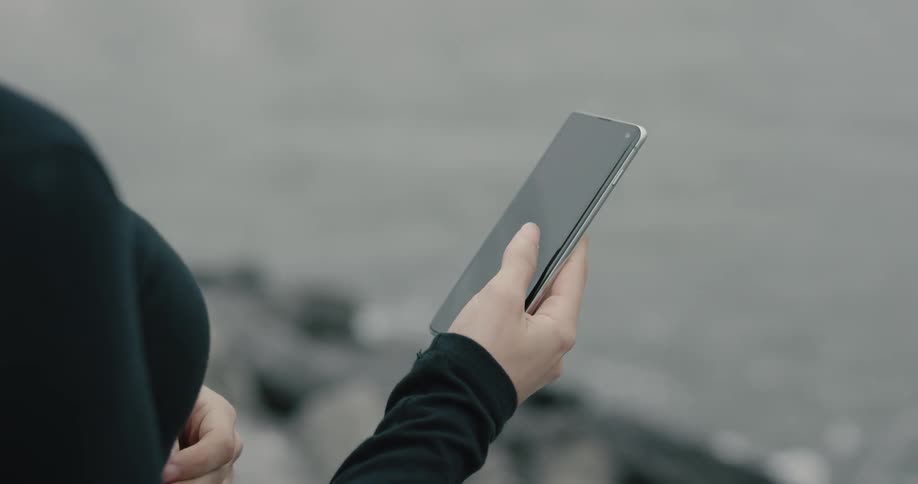 A woman uses her smartphone while standing above a body of water