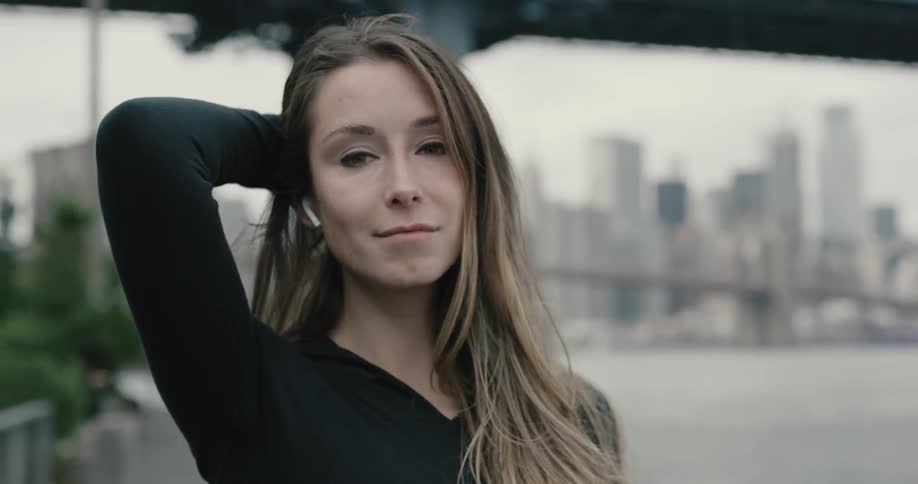 A woman puts in her wireless bluetooth headphone and pushes her long hair back and smiles