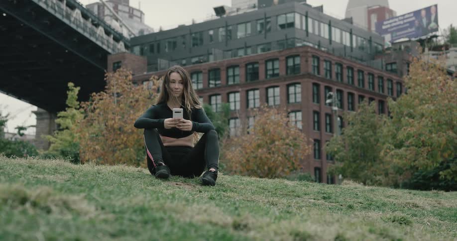 A young woman sits on a hill and looks at her cell phone