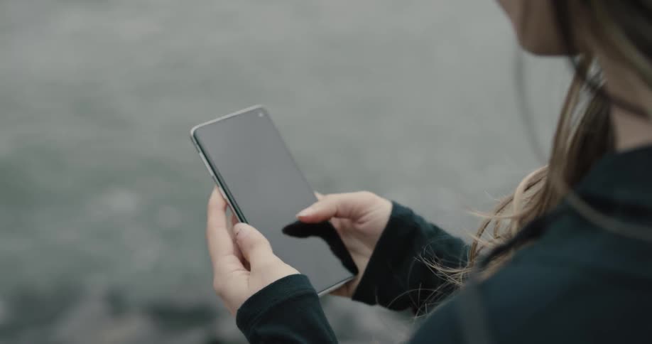 Woman wearing earphones uses smartphone next to the river on a cloudy day