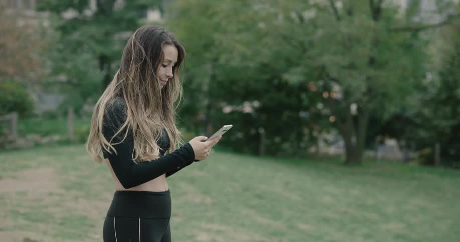 A young woman walks along and stops and looks at her phone