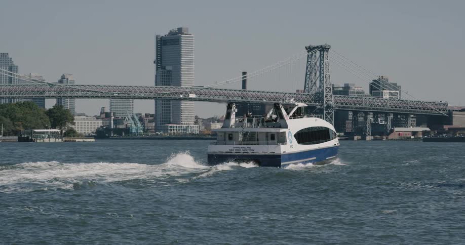 A boat carries people across the river by a city