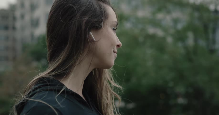 A young girl with ear pods in brushes her hair back and removes her ear pods